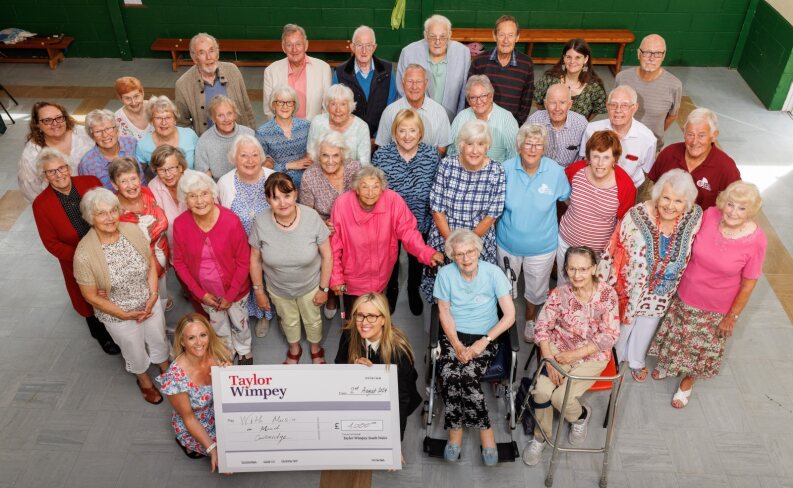 A photograph of around thirty members of Cowbridge singing group accepting a large presentation cheque for £1000 from Taylor Wimpey